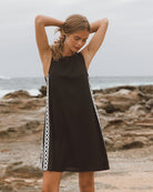 Woman wearing a black dress with white trim on a rocky beach.