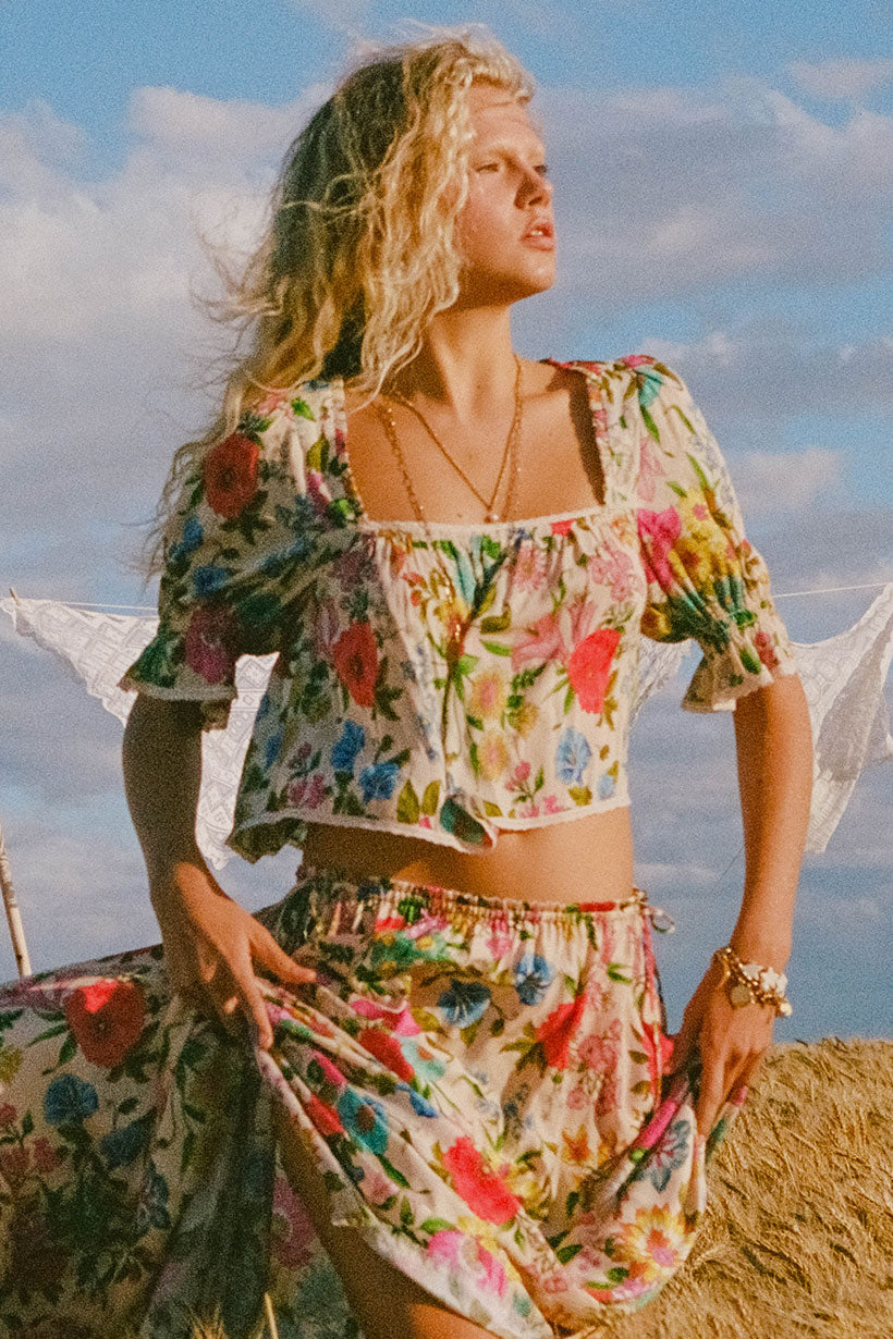 Woman in a floral outfit standing outdoors with a blue sky and clouds in the background