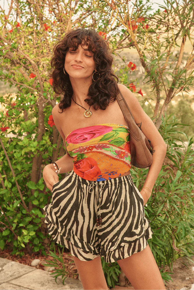 Woman wearing a colorful top and zebra print shorts standing in a garden.