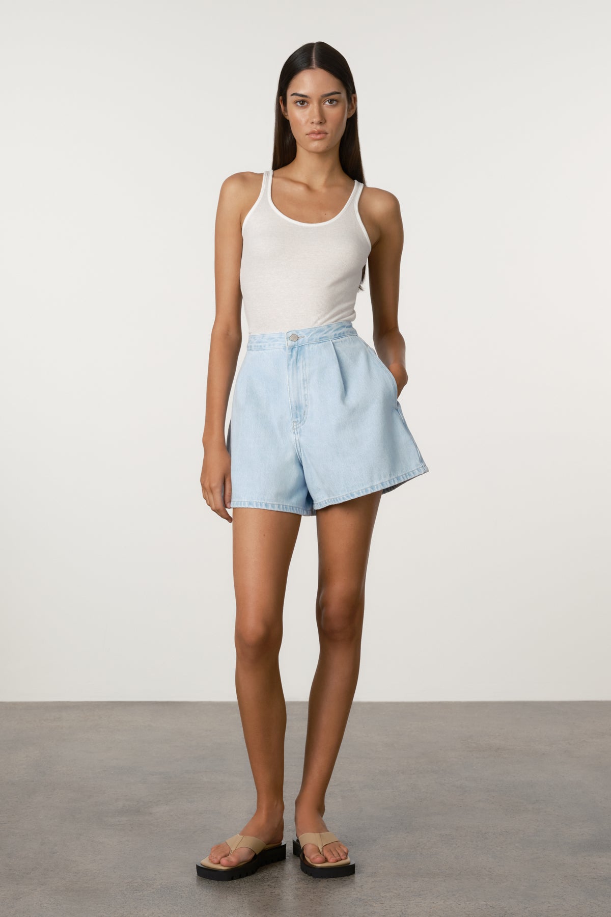 Woman wearing a white tank top and light blue shorts on a plain background