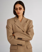 Woman wearing a beige suit with sunglasses on a plain background