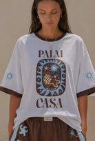 Person wearing a Palm Collective Maroc t-shirt in white with brown sleeve trim and brown and blue decorations