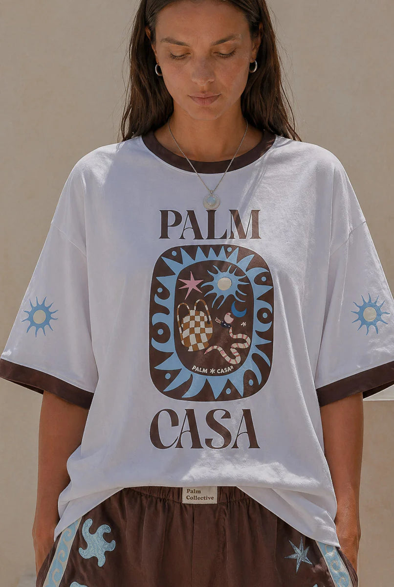 Person wearing a Palm Collective Maroc t-shirt in white with brown sleeve trim and brown and blue decorations