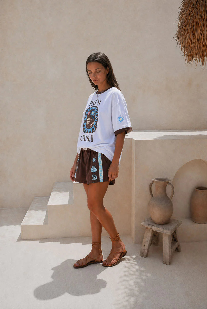 Person wearing a Palm Collective Maroc t-shirt in white with brown sleeve trim and brown and blue decorations