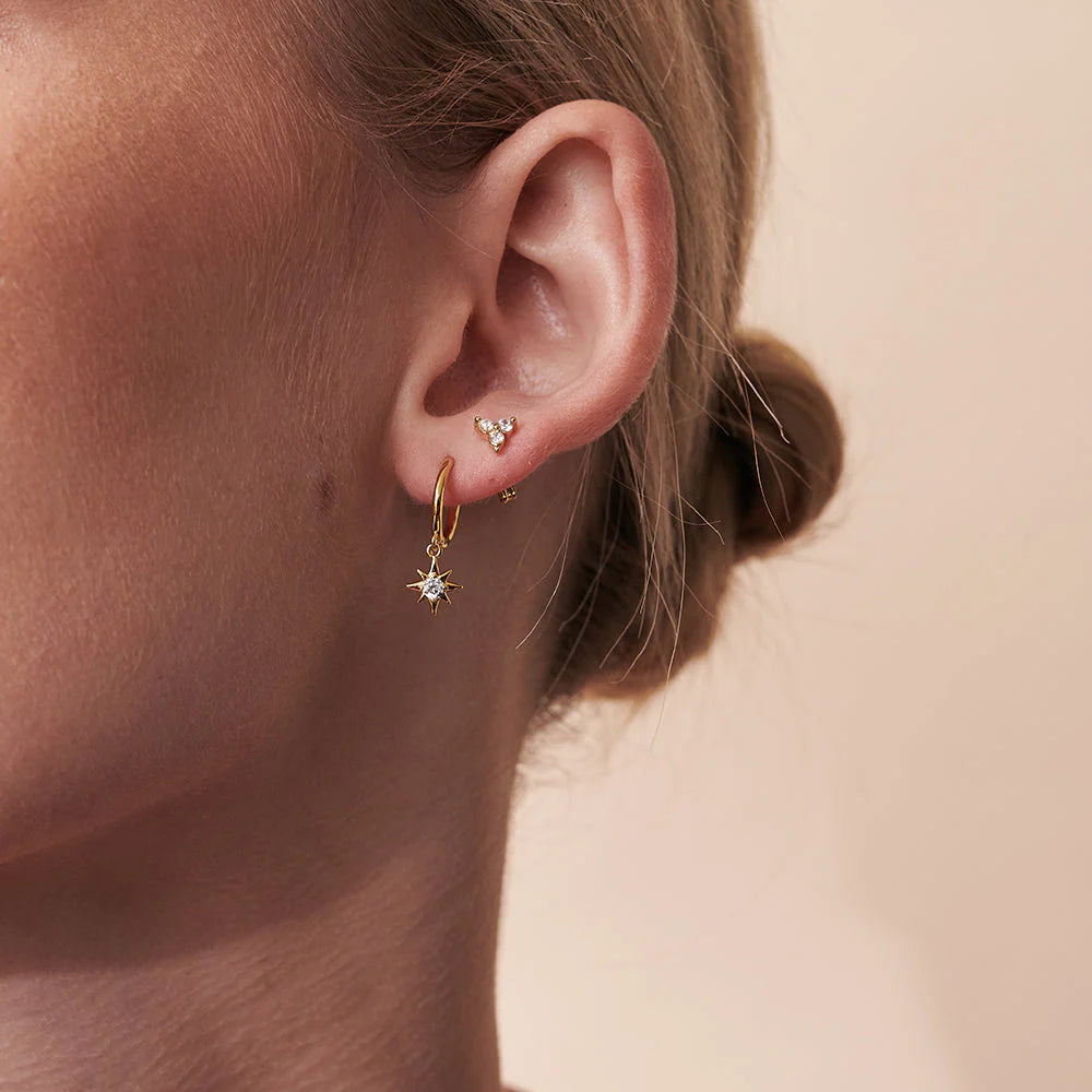 Close-up of a person wearing gold hoop earrings with small diamonds on a beige background