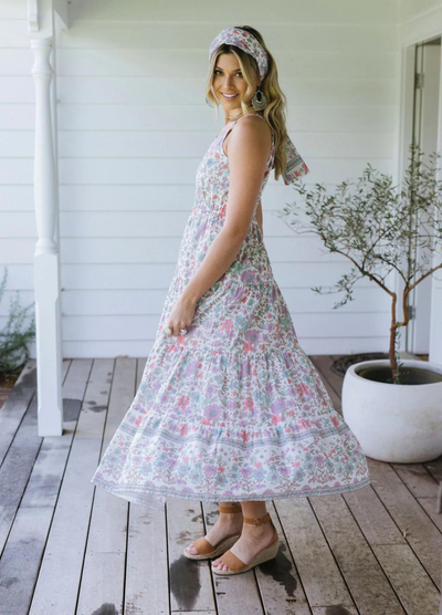 Blonde model wearing the house of skye bloom maxi dress a border print dress with straps and a floral print design in lilac