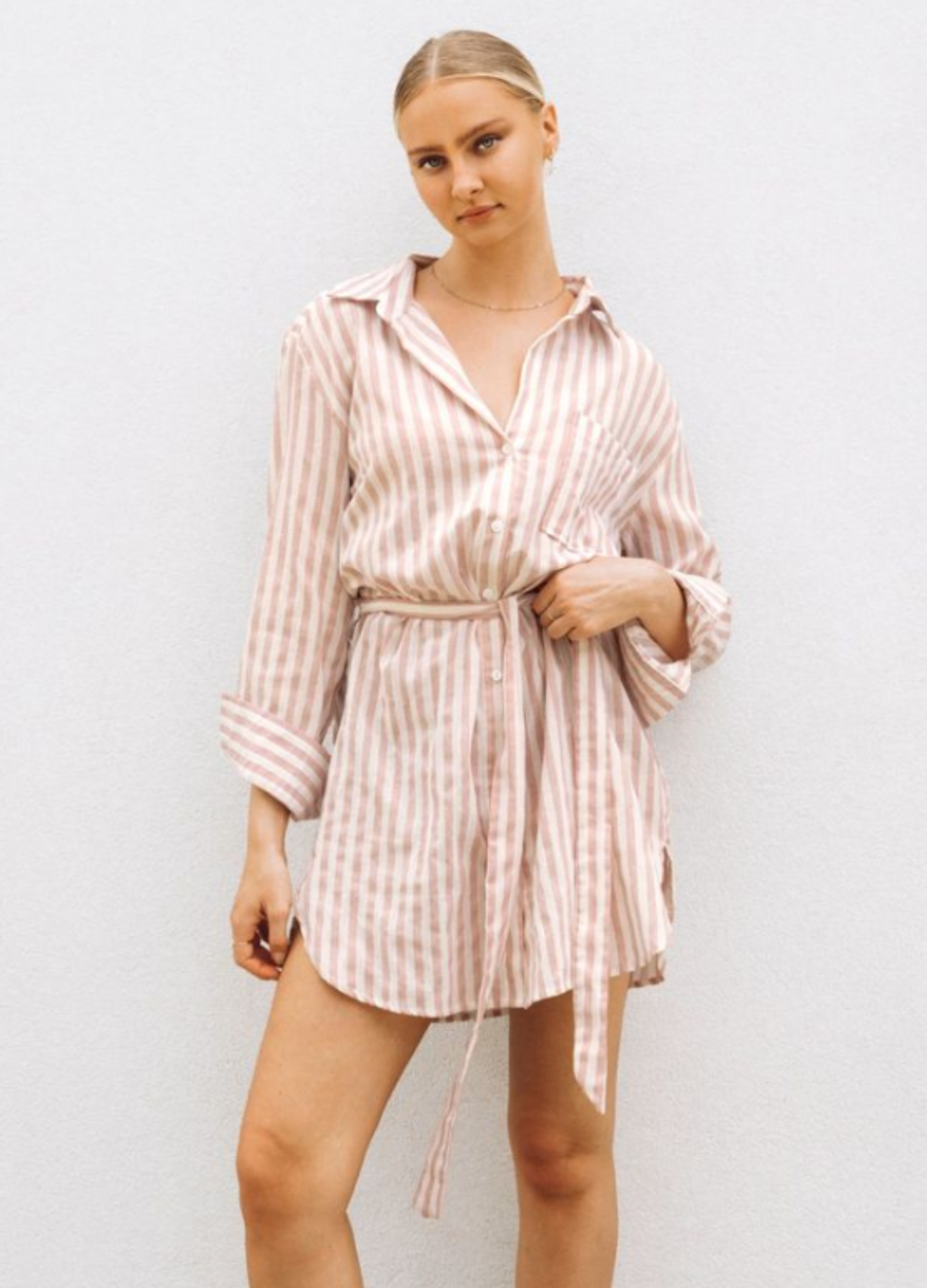 Model wearing soft pink stripe shirt dress with functional button placket, collar and belt
