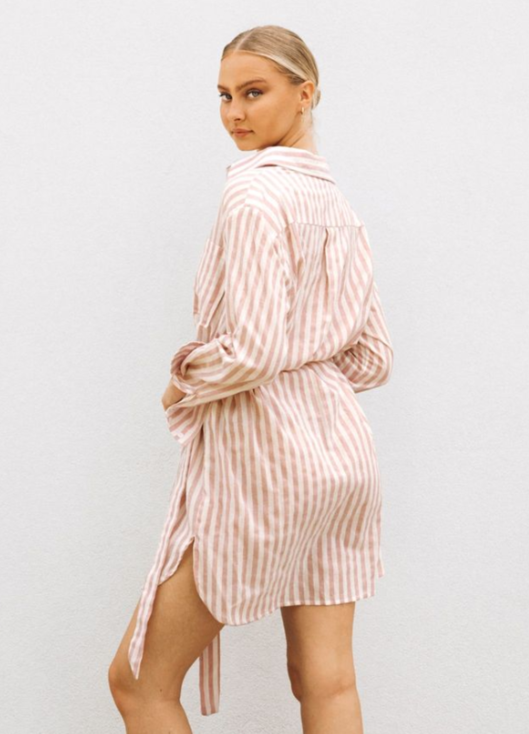 Model wearing soft pink stripe shirt dress with functional button placket, collar and belt