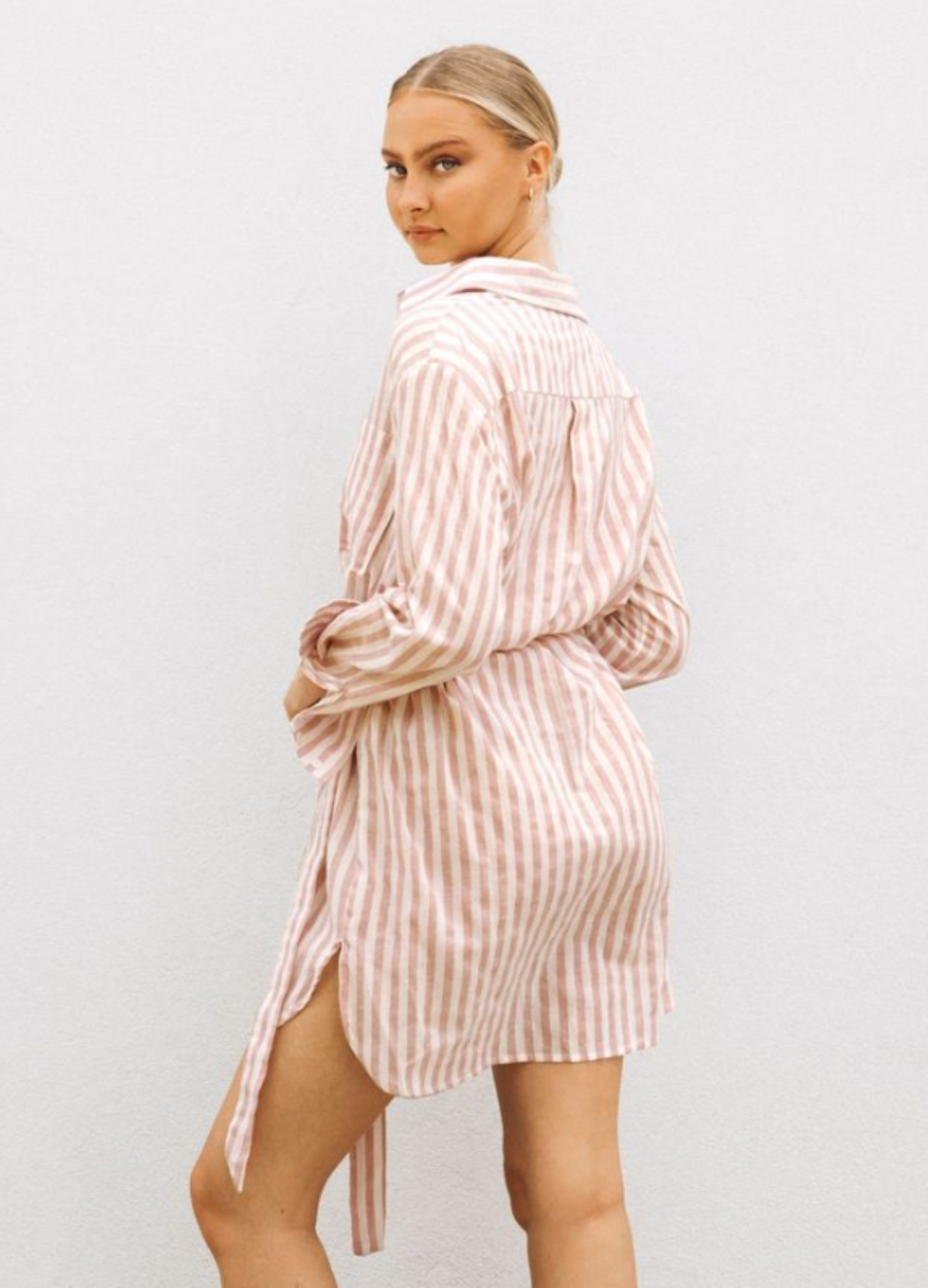Model wearing soft pink stripe shirt dress with functional button placket, collar and belt