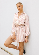 Model wearing soft pink stripe shirt dress with functional button placket, collar and belt