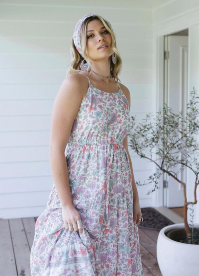 Blonde model wearing the house of skye bloom maxi dress a border print dress with straps and a floral print design in lilac