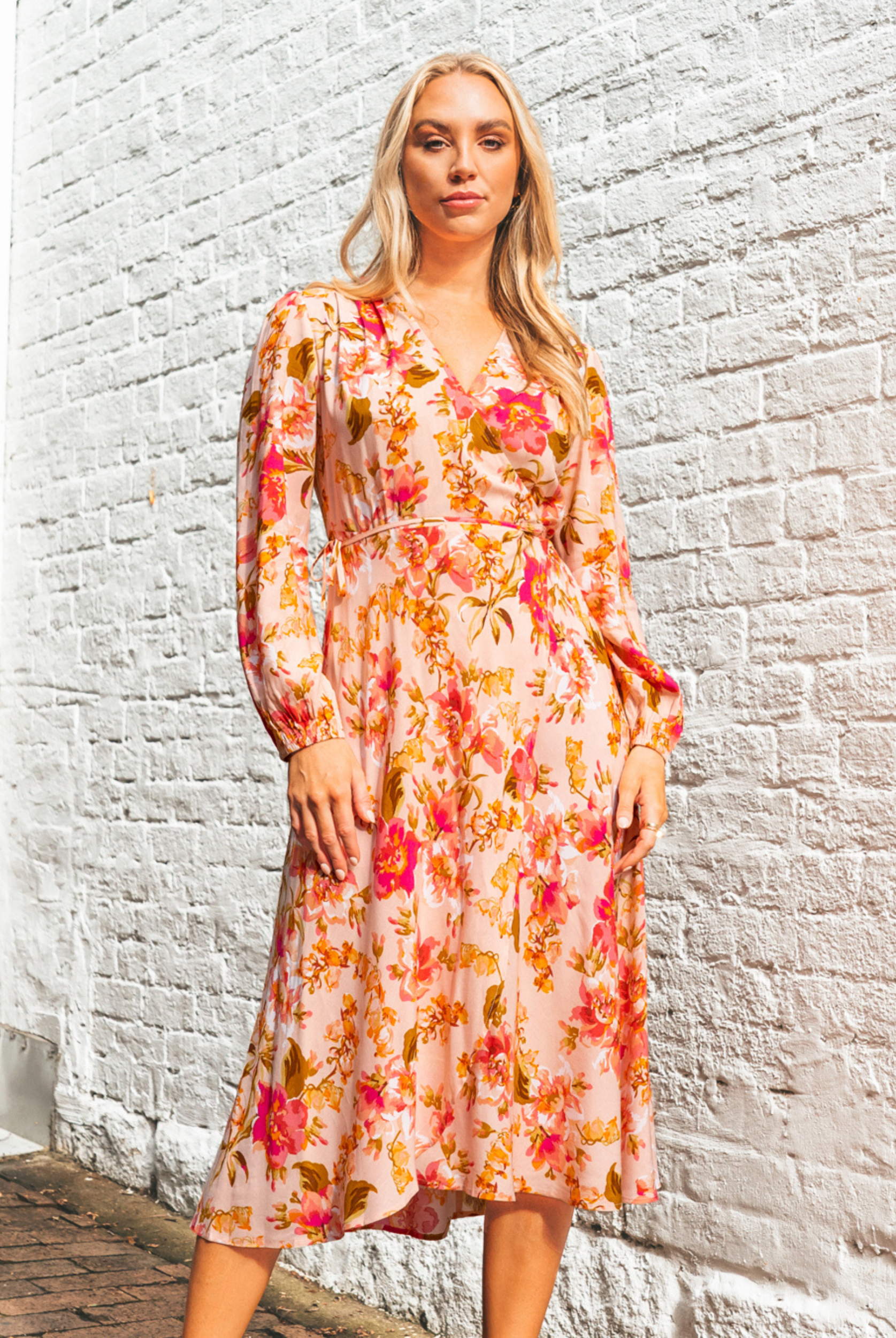 Blonde model wearing the Calla Rose Midi Dress in Pink Print with wrap style, long sleeve and tie waist