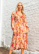 Blonde model wearing the Calla Rose Midi Dress in Pink Print with wrap style, long sleeve and tie waist