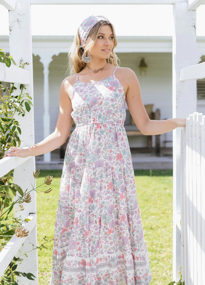 Blonde model wearing the house of skye bloom maxi dress a border print dress with straps and a floral print design in lilac
