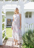 Blonde model wearing the house of skye bloom maxi dress a border print dress with straps and a floral print design in lilac