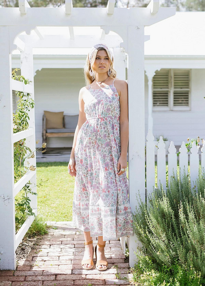 Blonde model wearing the house of skye bloom maxi dress a border print dress with straps and a floral print design in lilac
