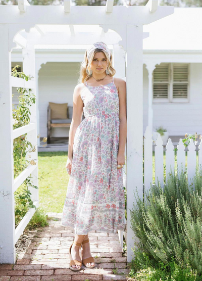 Blonde model wearing the house of skye bloom maxi dress a border print dress with straps and a floral print design in lilac