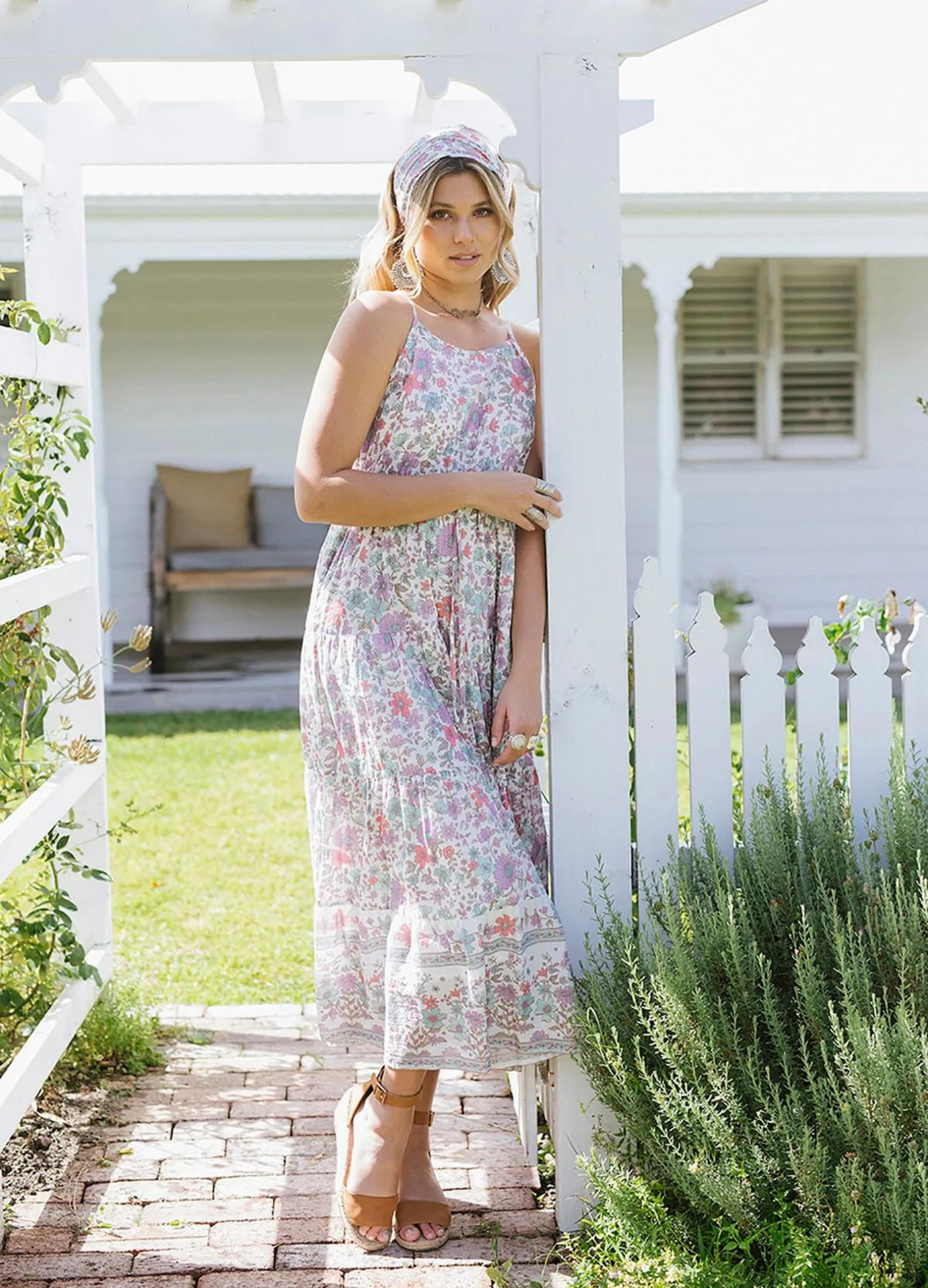 Blonde model wearing the house of skye bloom maxi dress a border print dress with straps and a floral print design in lilac