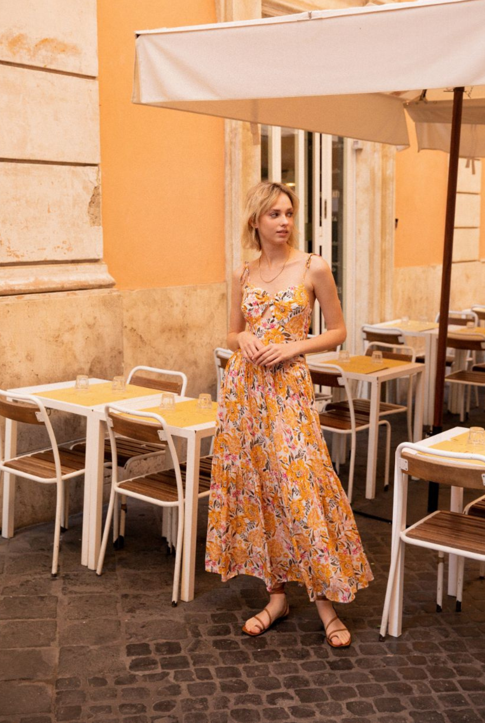 Model wearing the floral printed ezra sundress standing against a wall with gold jewellery