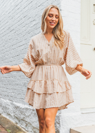 Model wearing neutral and white gingham shirt dress with functional button placket and elasticated waistband