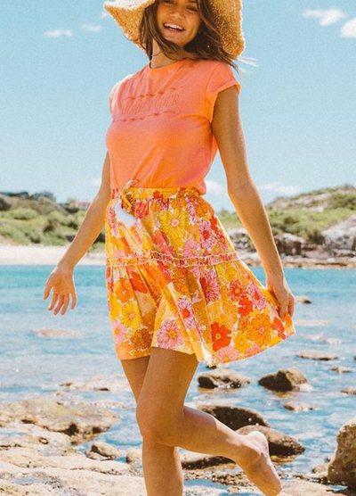 Woman on beach wearing orange tee and floral skirt