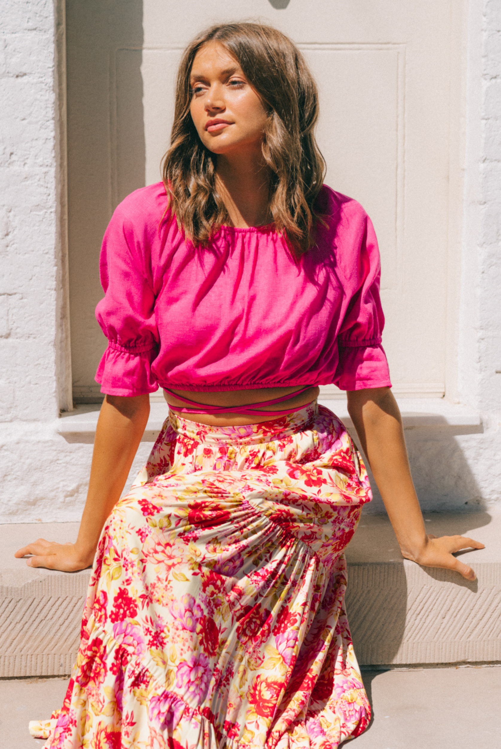 Model wearing the Riley Bright pink top and sitting down on a step