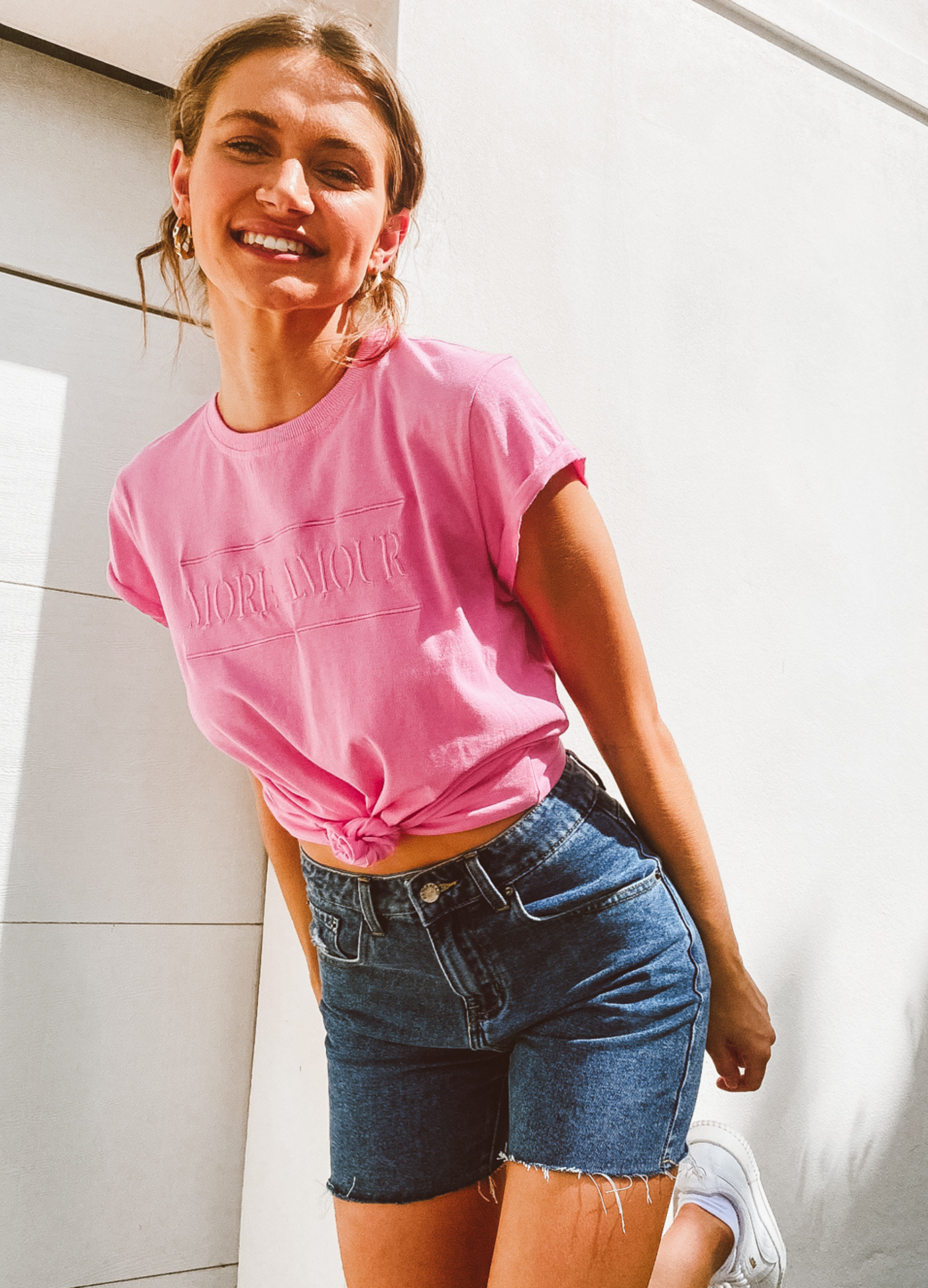 Women smiling and wearing a pink tshirt and denim cut off shorts