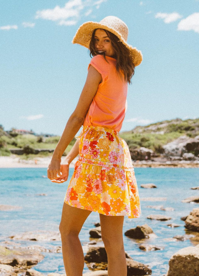 Woman wearing orange tee and floral skirt from behind