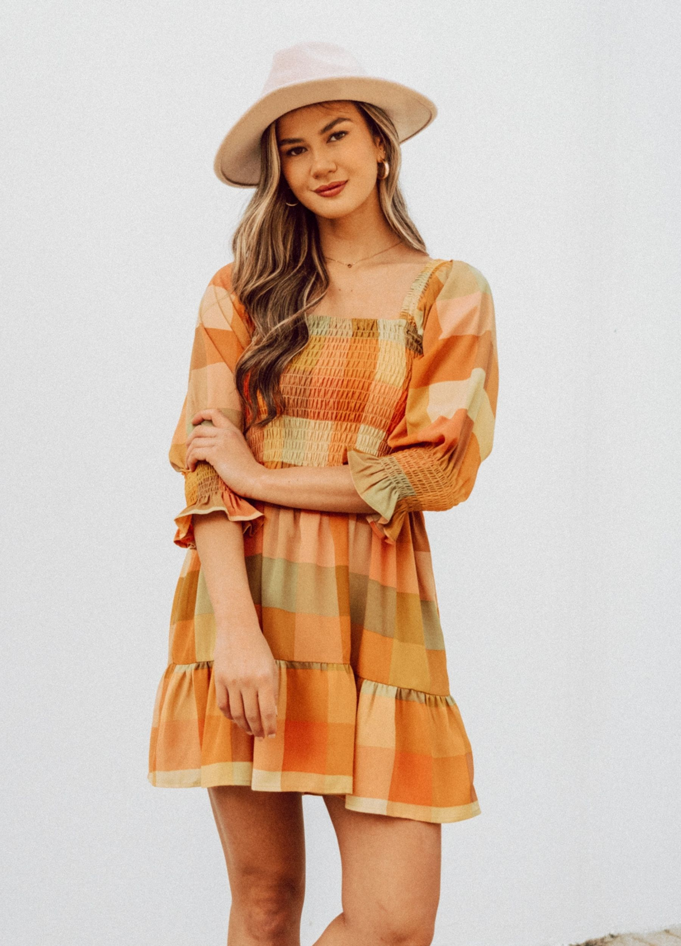 Woman wearing check mini dress in orange and khaki colourway with hat