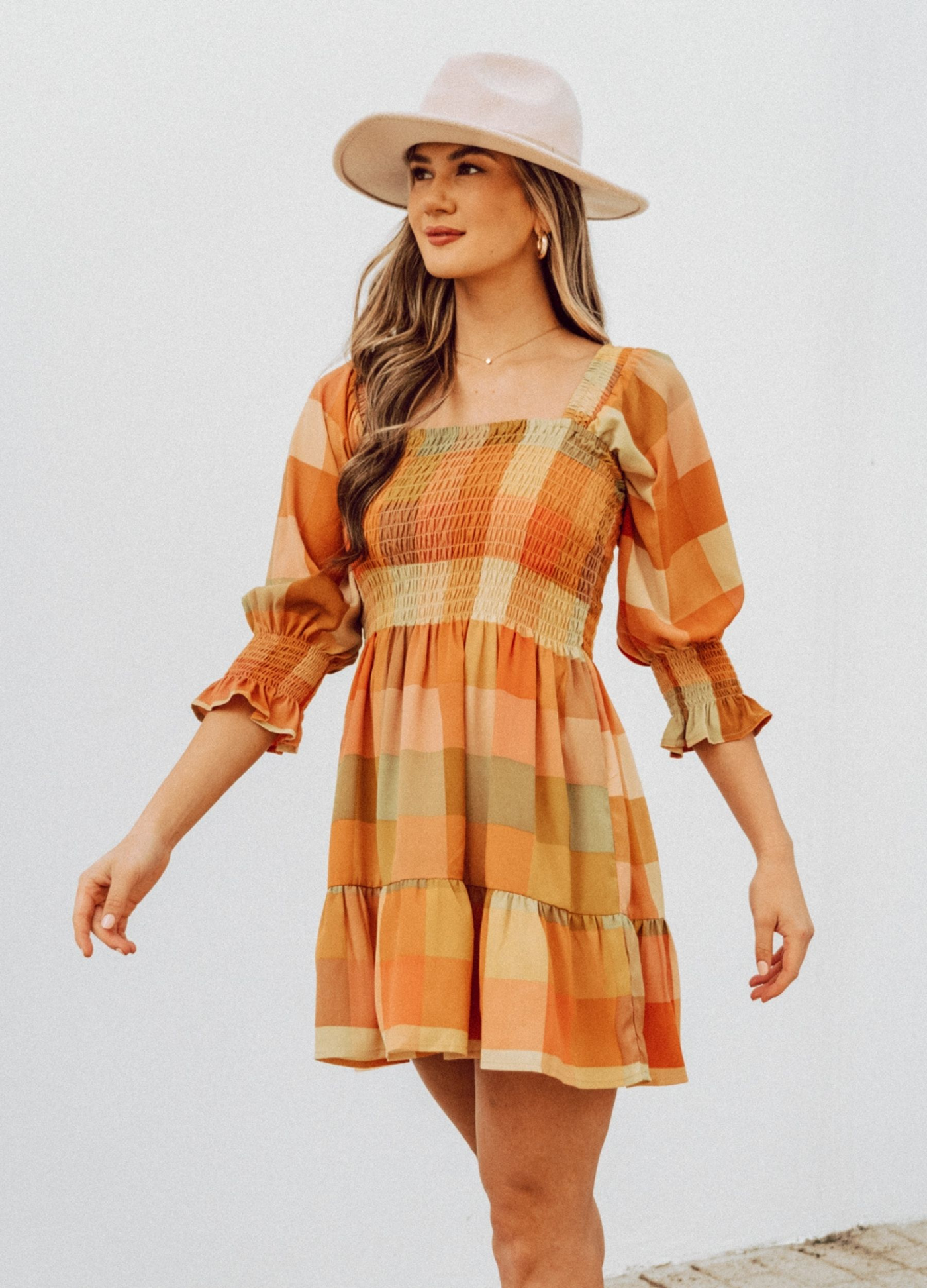 Woman wearing check mini dress in orange and khaki colourway with hat