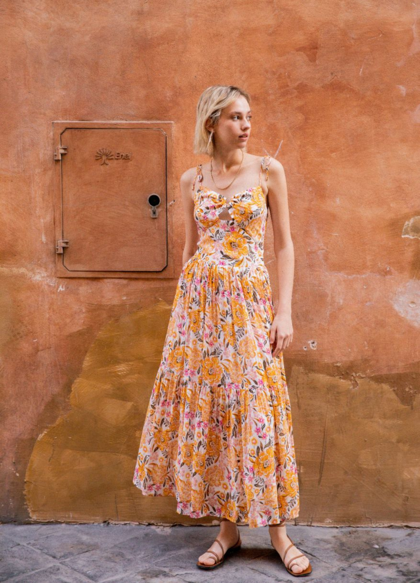Model wearing the floral printed ezra sundress standing against a wall with gold jewellery
