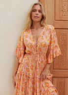 Model wearing orange floral print gown with button front and drawstring tie at waist with a mid length sleeve