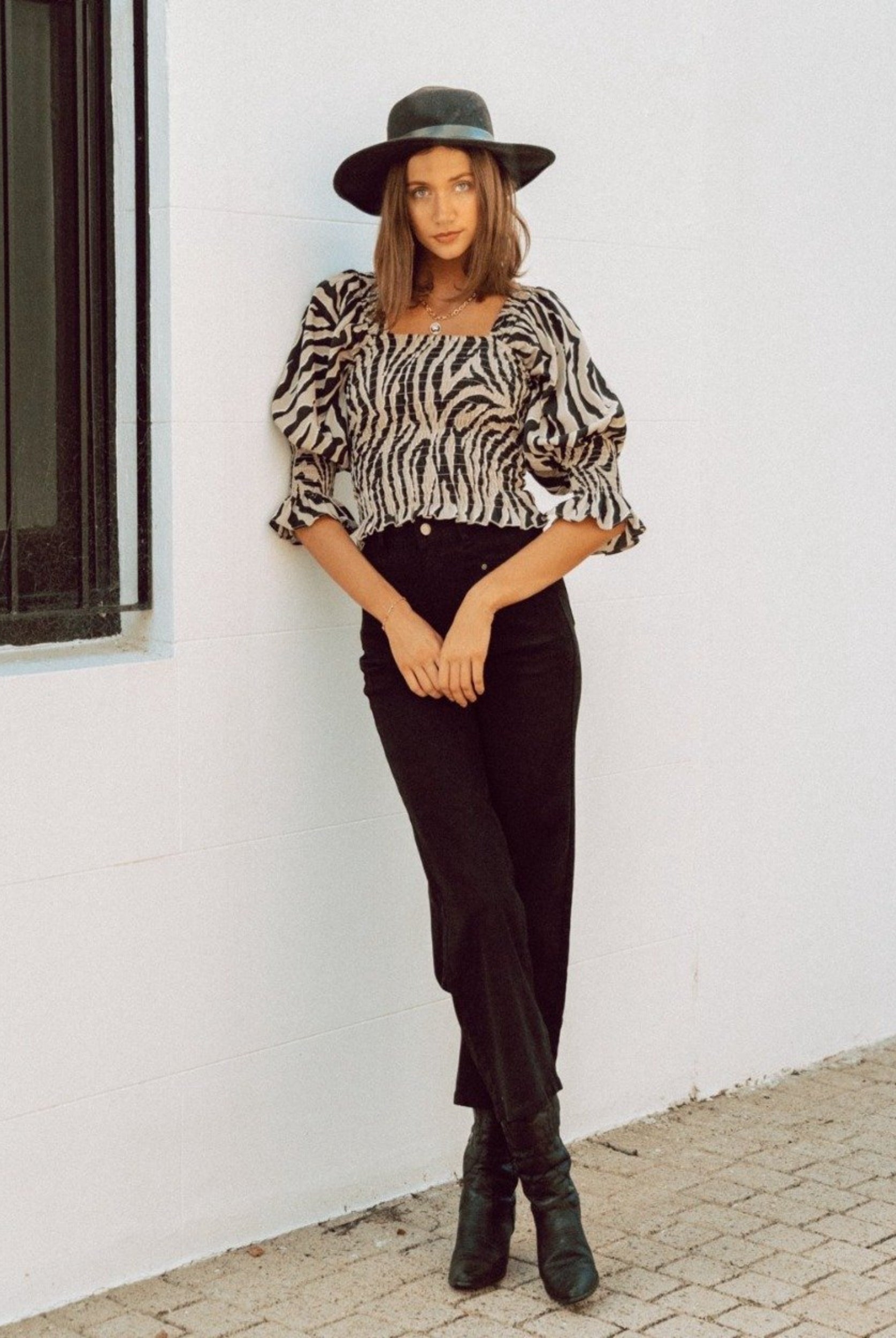 Woman wearing animal print top with black hat and black jeans