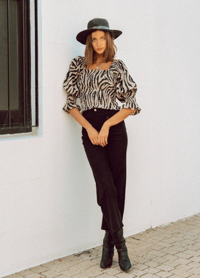 Woman wearing animal print top with black hat and black jeans