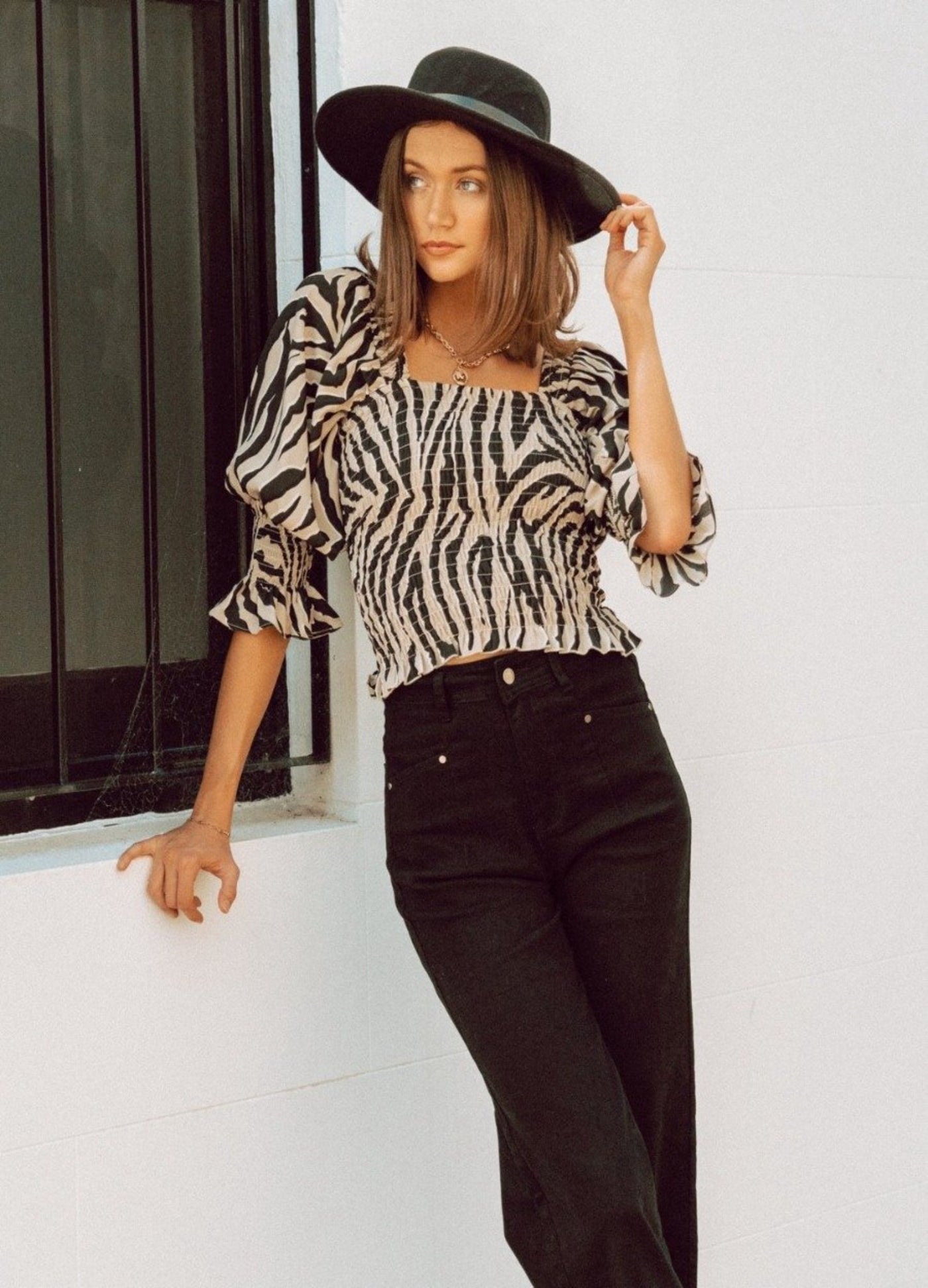 Woman wearing animal print top with black hat and black jeans