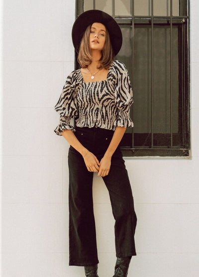 Woman wearing animal print top with black hat and black jeans