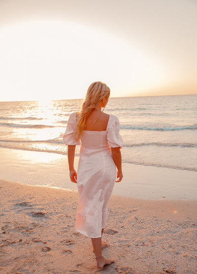 Blonde model wearing pale pink monte dress on a beach