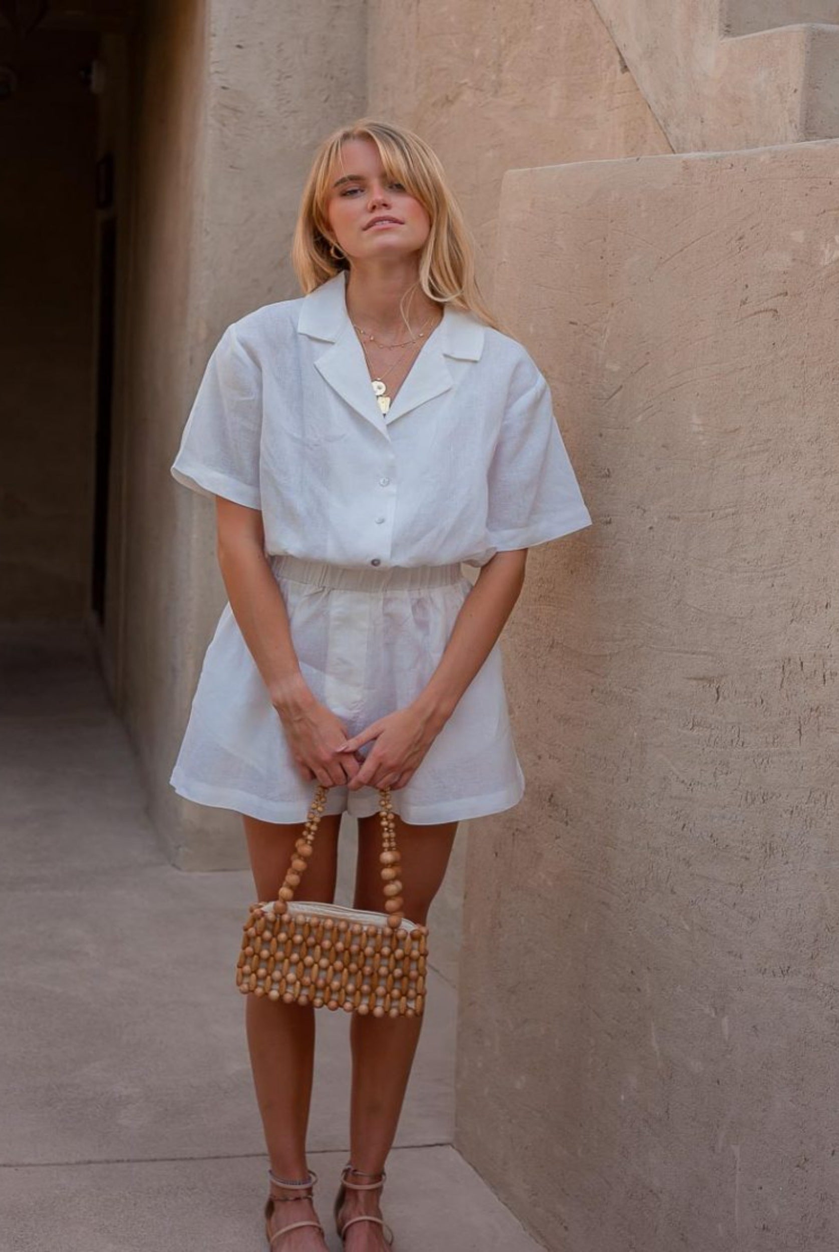 Blonde woman wearing white playsuit in 100% linen and holding a raffia bag