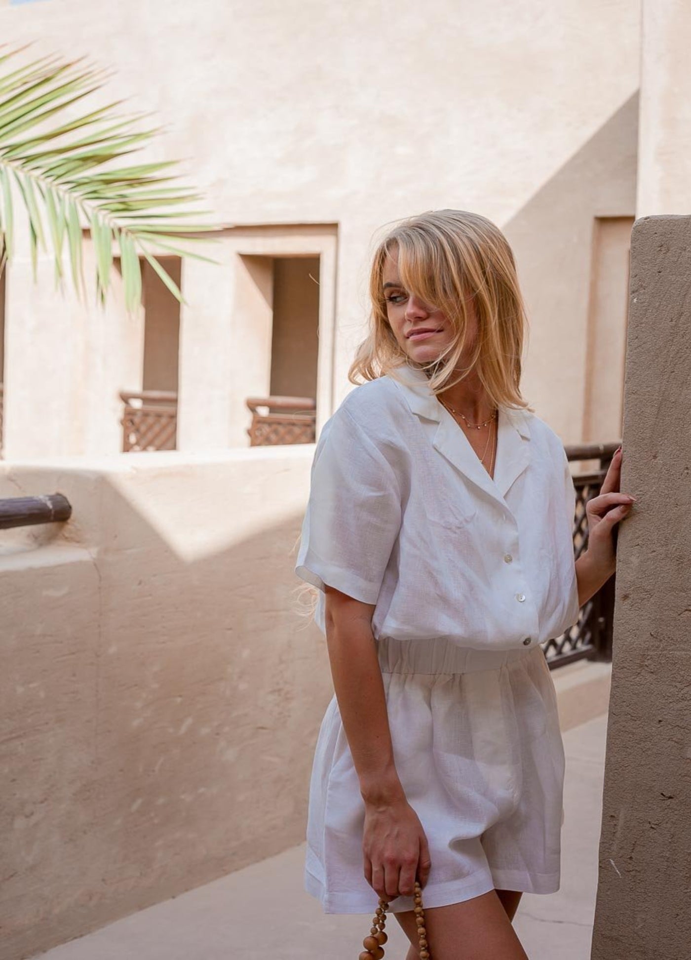 Blonde woman wearing white playsuit in 100% linen and holding a raffia bag